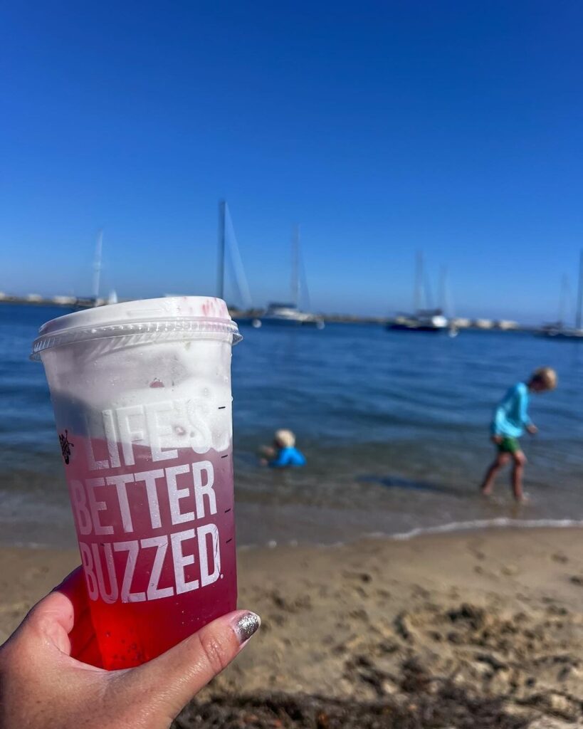someone holding a chilled beverage while children play on the beach in the background