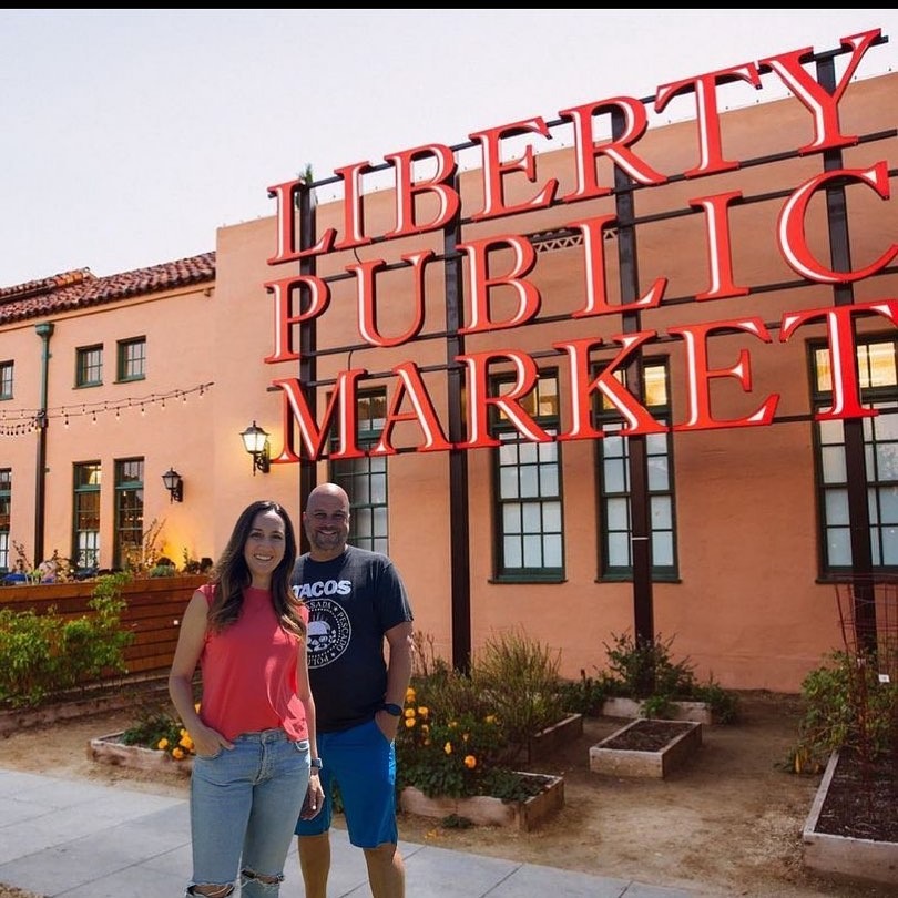 A man and woman standing in front of the Liberty Station sign